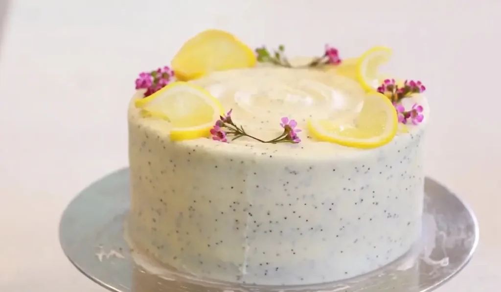 "A close-up of a lemon poppy seed loaf cake with a light lemon glaze and garnished with fresh lemon slices and edible flowers."